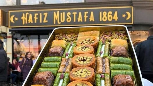 Je regarde un plateau de pâtisseries turques chez Hafiz Mustafa 1864 à Istanbul, avec des loukoums verts, des baklavas au miel et des gâteaux à la pistache joliment disposés.