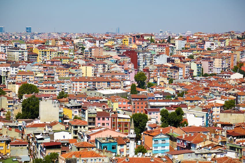 Panorama urbano di Istanbul con migliaia di edifici multicolori (piastrelle rosse, rosa, gialle, blu, verdi) densamente concentrati su colline ondulate. Sono visibili i quartieri di Beyoğlu, Aksaray e Fatih, le mura storiche meridionali e il Bosforo sullo sfondo. Metropoli transcontinentale su due continenti (Europa-Asia) fondata su 7 antiche colline.