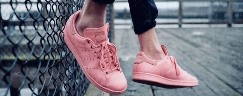 Pair of pink sneakers worn by a person sitting along a railing on a wooden dock.