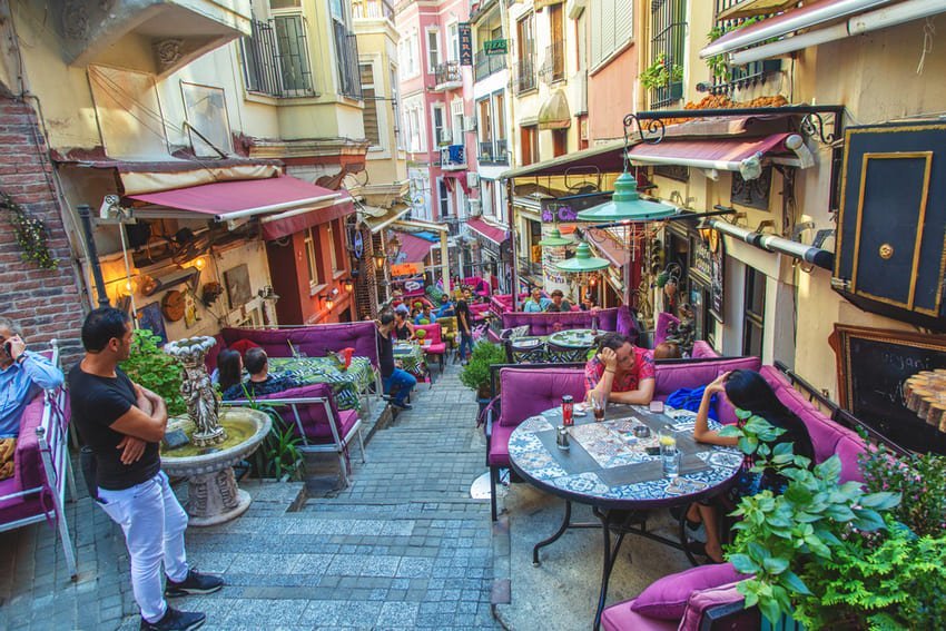 Rue typique en escalier dans le quartier bohème de Cihangir ou Galata à Istanbul, bordée de terrasses de cafés colorées et animées.