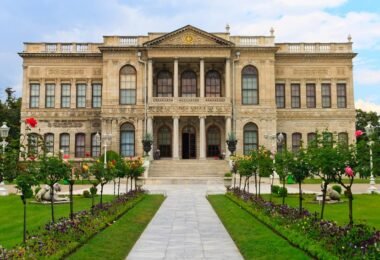 I look at Dolmabahçe Palace, a 19th-century building in Istanbul, with its symmetrical façade, columns and flower garden lined with lion statues.