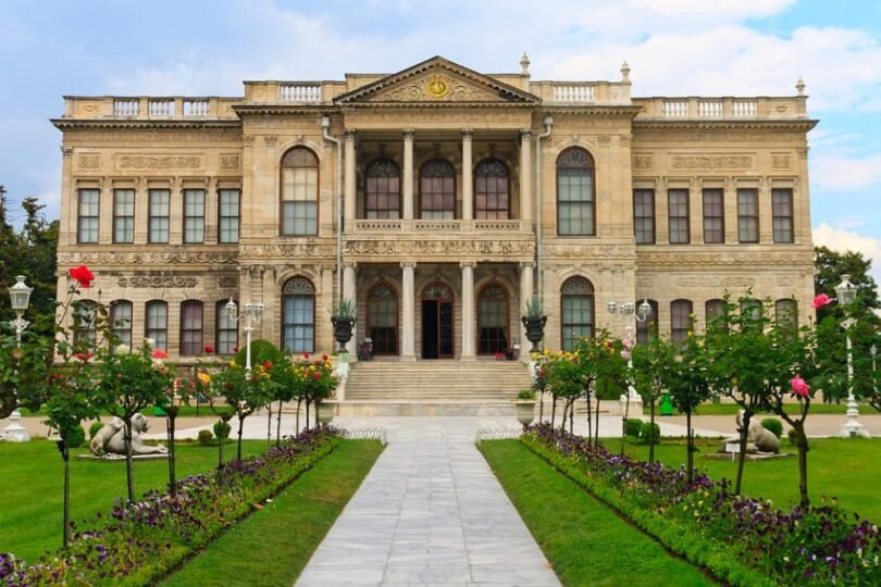 I look at Dolmabahçe Palace, a 19th-century building in Istanbul, with its symmetrical façade, columns and flower garden lined with lion statues.