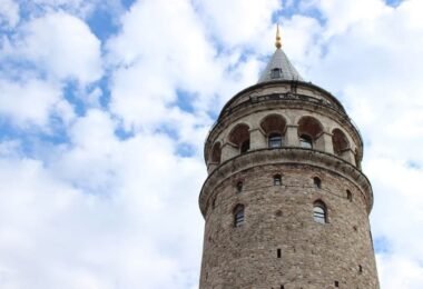 I am facing the Galata Tower seen from a low angle, with its arches and spire; built in 1348, it peaks near 67 m, a historical lookout of Istanbul.