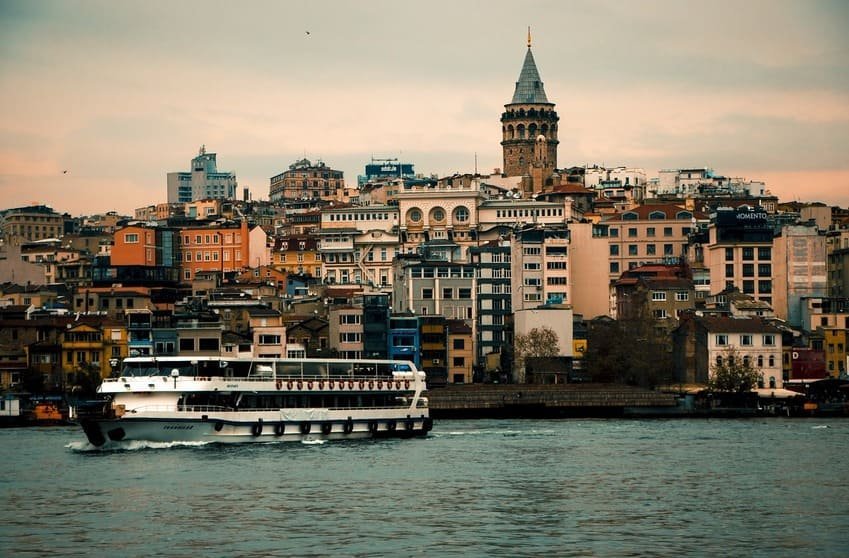 Je fais face à Karaköy vu depuis l'eau, un vapur passe au premier plan ; la tour de Galata, construite en 1348, culmine à près de 67 m, un monument historique d'Istanbul.