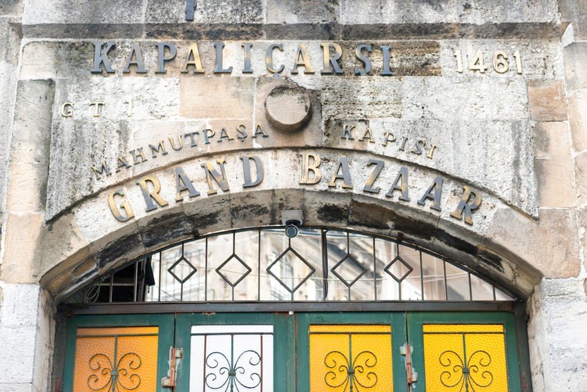 Entrée en pierre du Grand Bazar d'Istanbul, inscription « Mahmutpaşa Kapısı » et date « 1461 » au-dessus d'une arche. Je me trouve face à cette porte du Kapalıçarşı, construite en 1461, qui s'ouvre sur un réseau de plus de 60 rues et près de 4 000 boutiques.