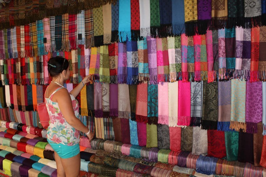 Une boutique du bazar où sont exposées des rangées de foulards et de châles multicolores suspendus au plafond, avec des rouleaux assortis posés au sol. Je regarde des pashminas fabriqués à partir d'un mélange de soie, de laine et de viscose, conçus pour être légers et chauds.