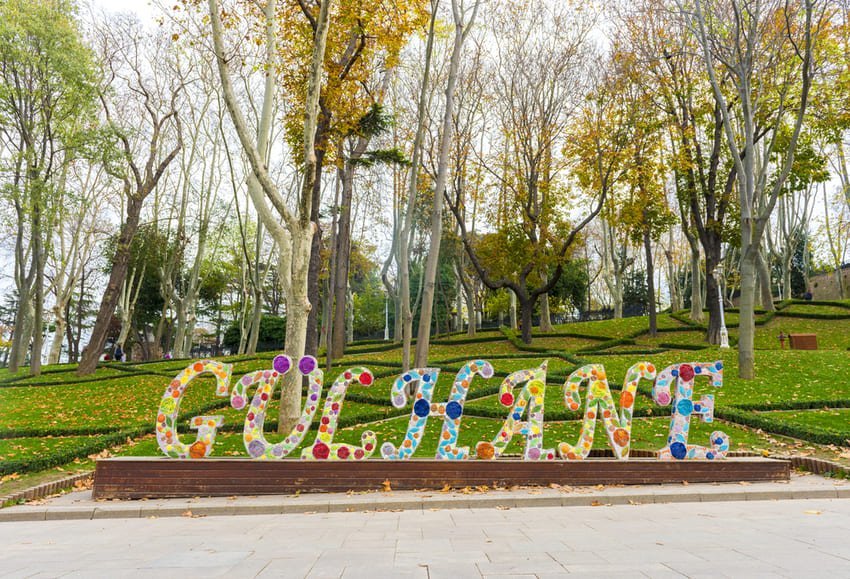 Entrée en lettres florales du parc Gülhane à Istanbul, grands arbres aux feuilles dorées d'automne, pelouse en terrasses et chemin pavé devant le parc.
