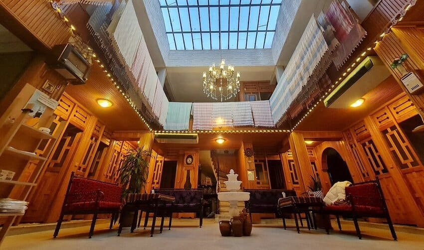 Je contemple l'intérieur du Pera Palace Hotel à Istanbul, un hôtel historique datant de 1895, de style Belle Époque, avec ses balcons en bois sculpté, ses lustres en cristal et sa verrière centrale.