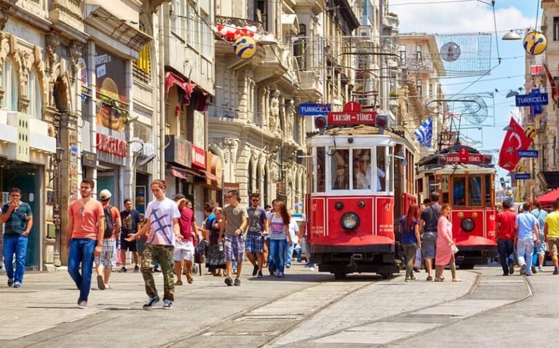 I walk along İstiklal, Istanbul's flagship avenue, where 19th-century red trams run through dense crowds against a backdrop of historic buildings.