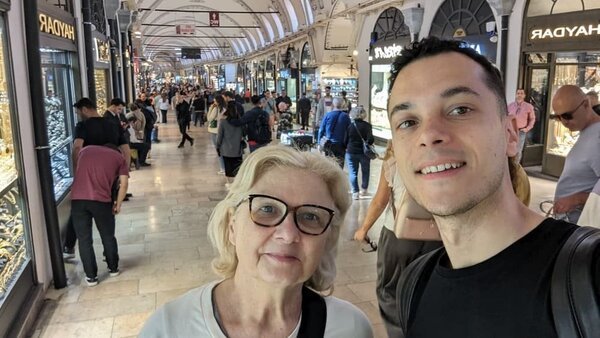 Kevin spaceruje z podróżnikiem po tętniącej życiem uliczce Wielkiego Bazaru w Stambule, otoczony oświetlonymi sklepami i przechodniami.