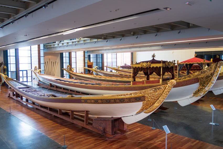 Sala espositiva del Museo Navale di Istanbul con 3 caicchi imperiali ottomani in legno dorato, spinti da remi. Barche reali lunghe e slanciate risalenti al XIX-XX secolo, con ornamenti in stile turco rosso-turchese sui lati. Interni moderni del museo con finestre a lucernario, collezione di 20.000 reperti navali che illustrano 6 secoli di potenza navale ottomana e turca.