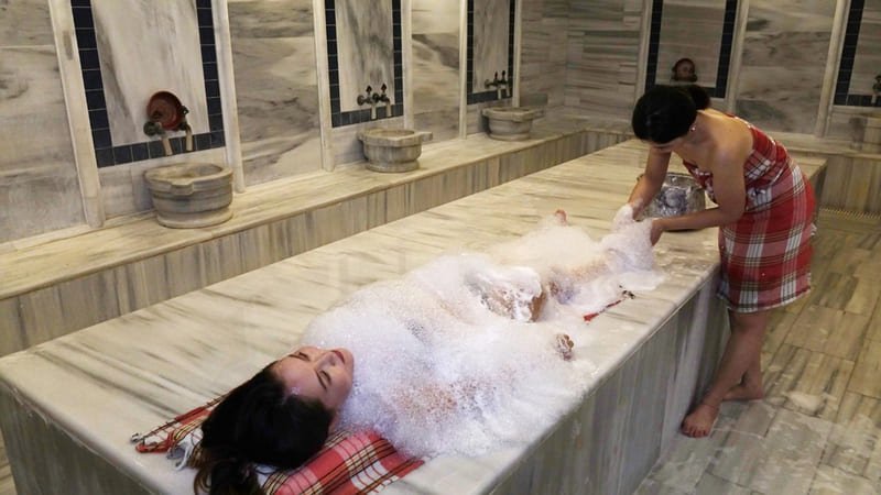 Kobieta leżąca na marmurze hammamu w Stambule podczas tradycyjnego masażu pianą w tureckiej łaźni